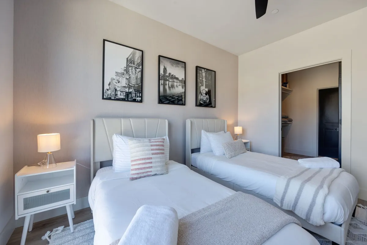 A cozy second bedroom outfitted with twin beds, complemented by matching table lamps and engaging wall art. The setup encourages both relaxation and shared moments, with a soft, inviting color palette that feels welcoming for friends or family.