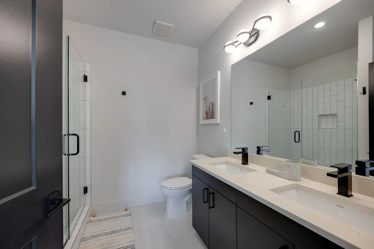A spacious, spa-inspired bathroom with a double sink vanity, sleek glass shower enclosure, a large mirror, and modern lighting. The clean lines and calming tones evoke a sense of relaxation and modern luxury.
