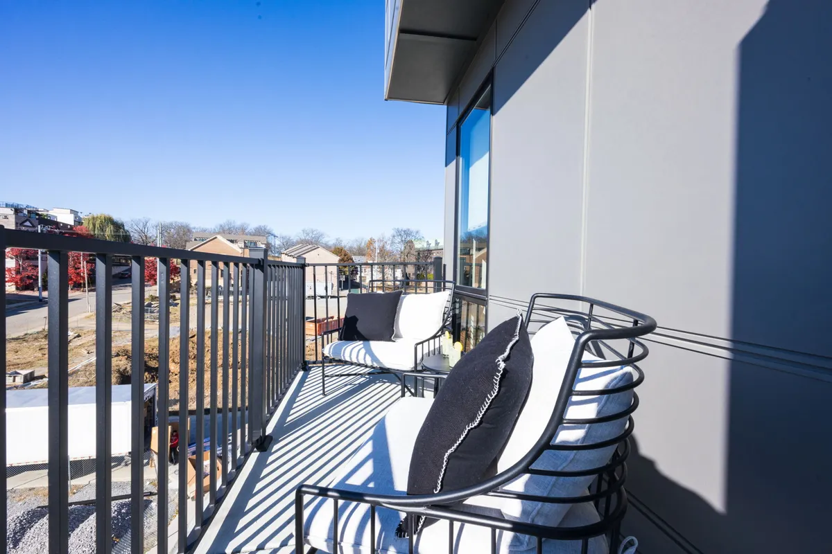 A private balcony with comfortable chairs and railings, offering a tranquil view of the surrounding area. The scene suggests a peaceful spot to enjoy coffee, drinks, or fresh air.