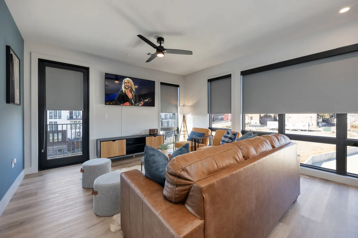 A cozy living space with a leather sofa, large TV, and oversized windows letting in abundant natural light. The room is inviting, ideal for relaxing, socializing, or enjoying family time after a busy day.
