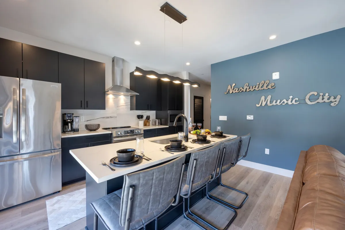 The image showcases the open-concept kitchen and dining area, featuring a spacious kitchen island with modern metallic appliances. The décor is bright and welcoming, with a focal Nashville Music City wall art piece, setting a vibrant and contemporary tone.
